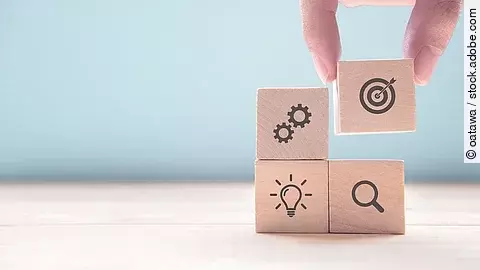 Hand stapelt Holzwürfel mit Strategiesymbolen darauf 