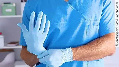 Krankenhauspersonal Person im blauen Kasack die sich Einmalhandschuhe anzieht