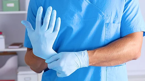 Person im blauen Kasack die sich Einmalhandschuhe anzieht